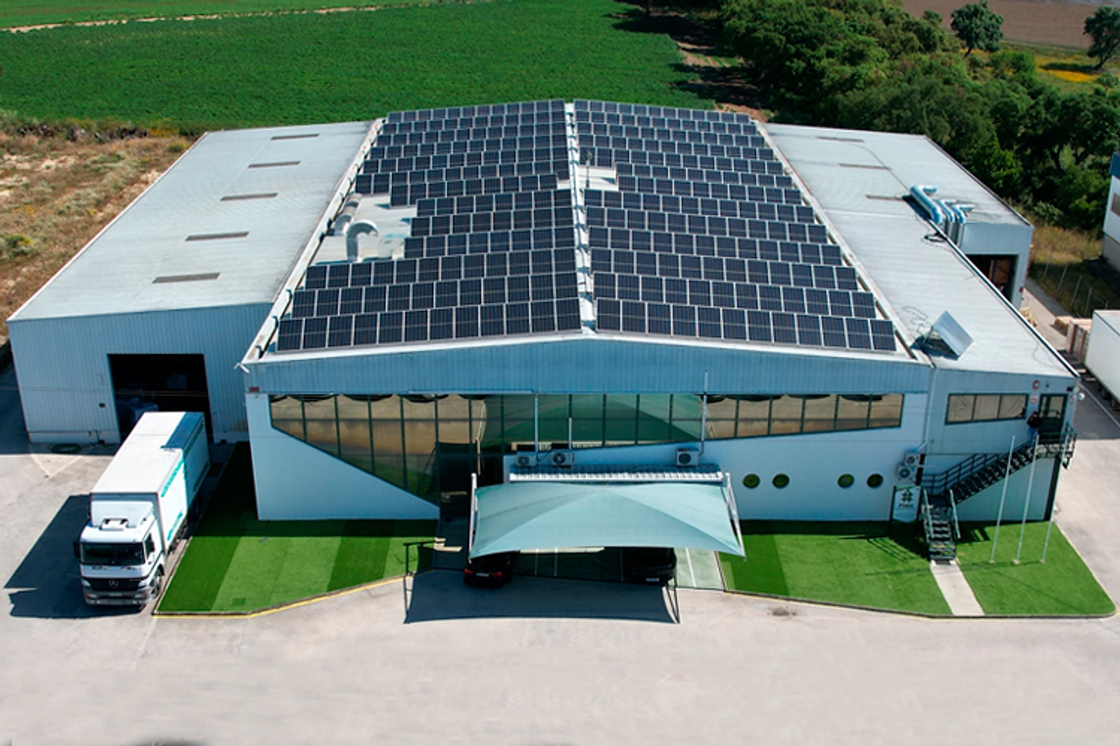 Aerial view of an industrial facility with rooftop solar panels surrounded by fields